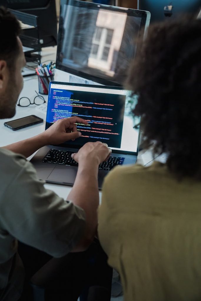 Two adults collaborating on programming tasks using a laptop in an office setting.