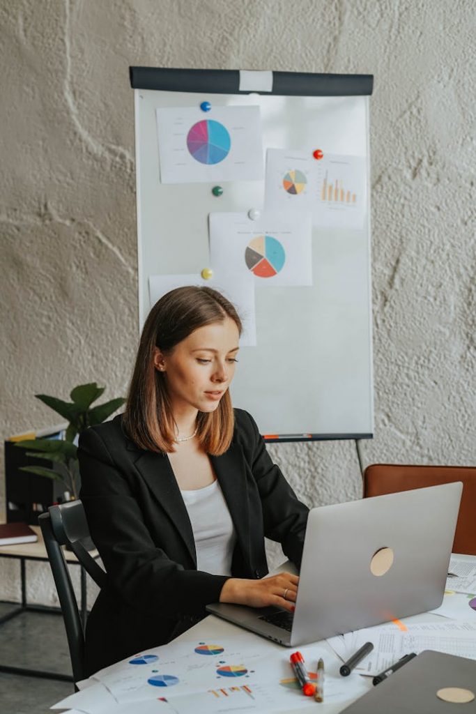 Confident businesswoman working on a laptop with charts in the background, focused on analysis.